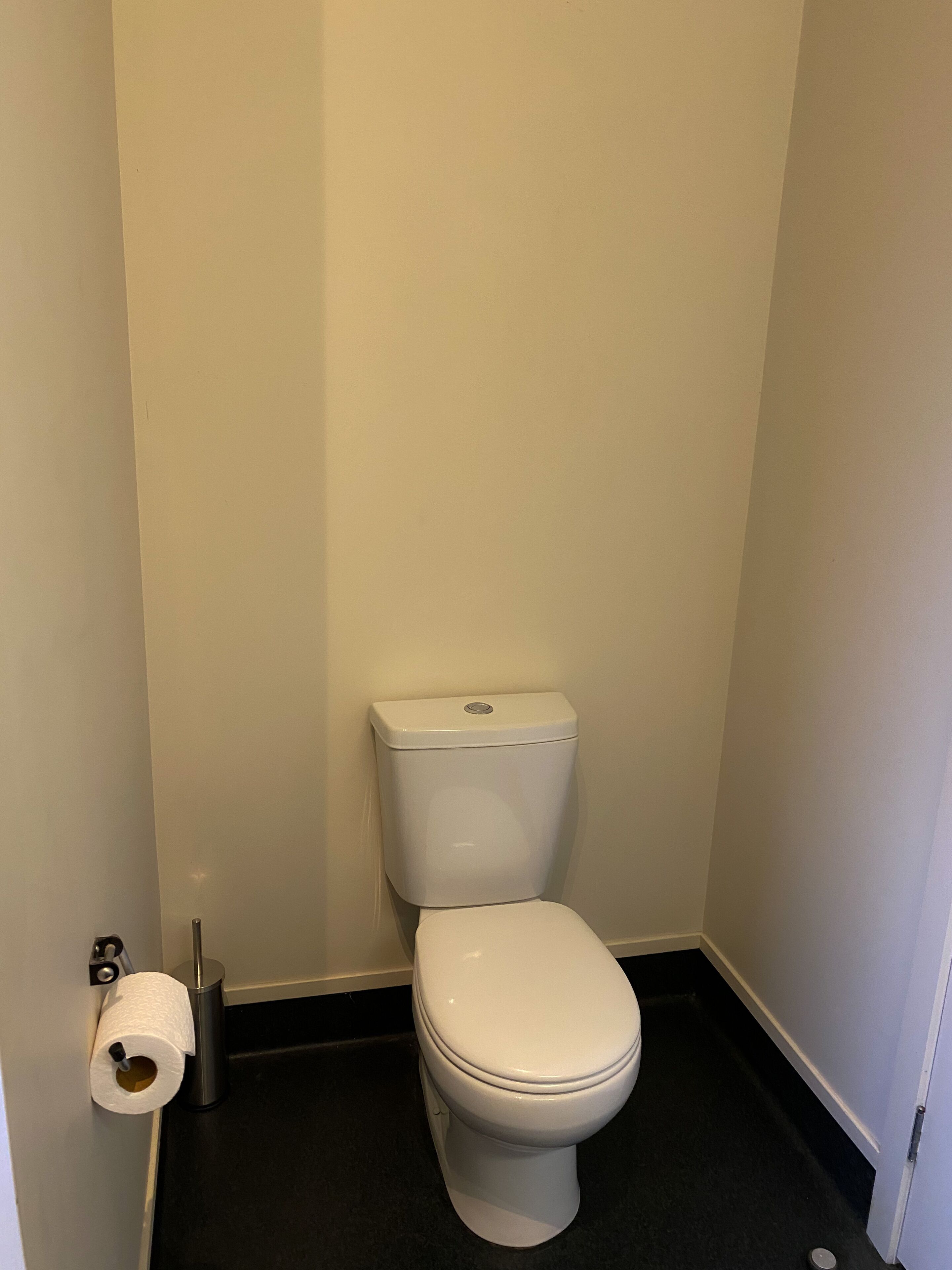A small, white toilet in a narrow bathroom with a black floor and white walls.