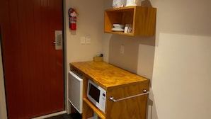 A compact kitchenette with a microwave, a small refrigerator, and a wooden shelf above holding dishes and a kettle. - Waitomo Lodge (Te Kuiti)