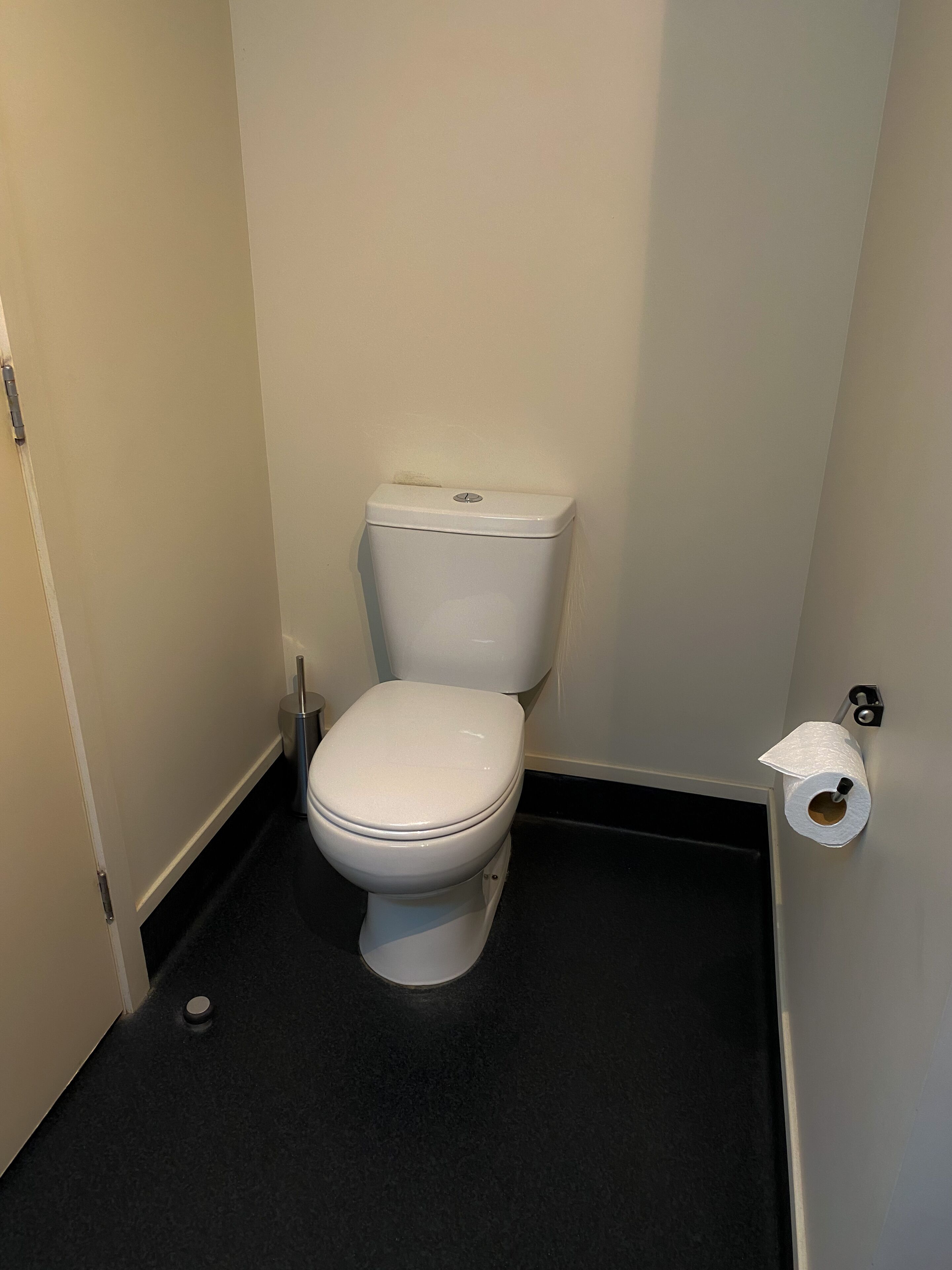 A small, compact bathroom with a white toilet, a black floor, and a toilet paper holder on the wall.