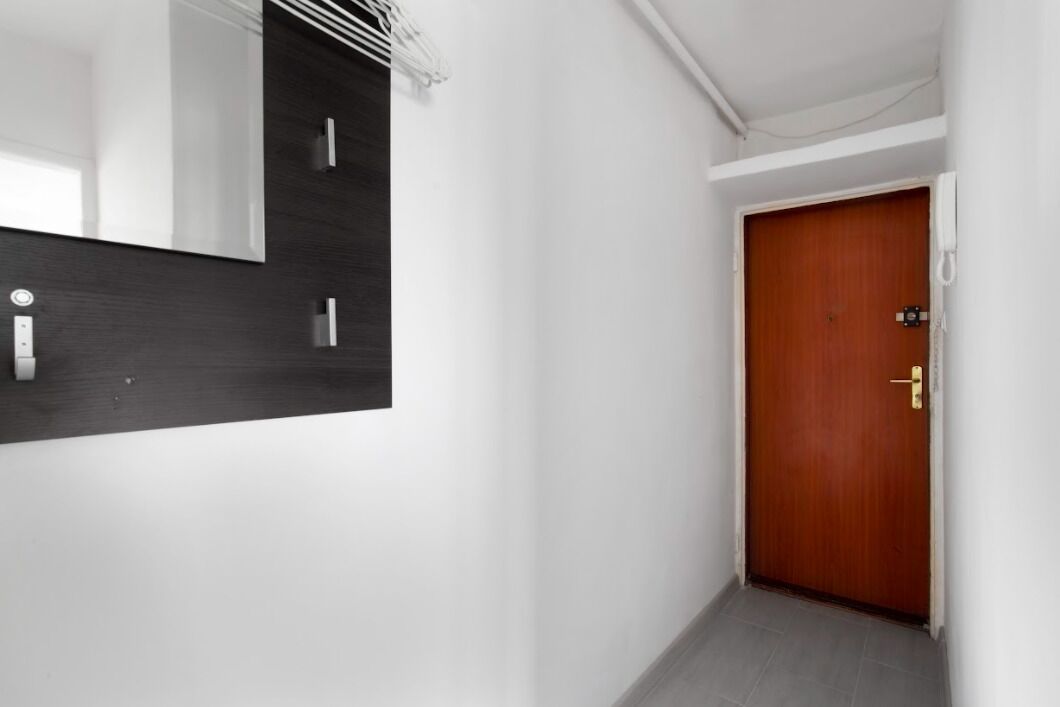 A narrow hallway with a wooden door and a mirror on the left wall.