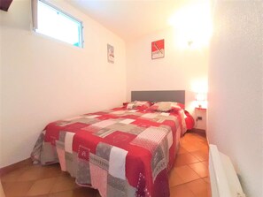 Un dormitorio con cama, mesita de noche, ventana y lámpara de pared.