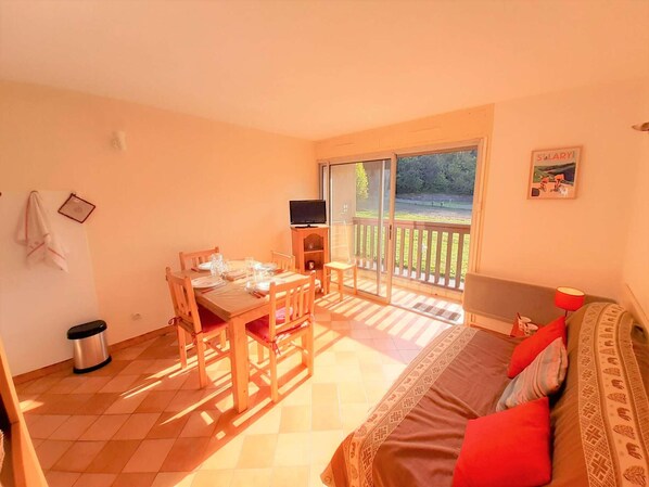 Un dormitorio con cama, una mesa con sillas, televisor y balcón con vistas al exterior.