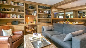 Ein gemütliches Wohnzimmer mit Ledersessel, grauem Sofa und Couchtisch mit Zeitschriften und einer Kerze.