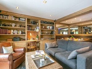 Ein gemütliches Wohnzimmer mit Ledersessel, grauem Sofa und Couchtisch mit Zeitschriften und einer Kerze.