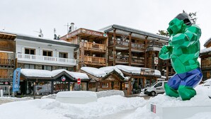 A snow-covered outdoor area with wooden buildings, a sign for 'La Saulce,' and a 'Grüne Pizza' restaurant.