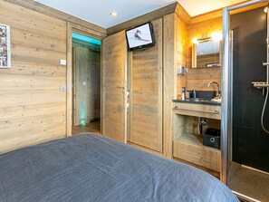 Ein Hotelzimmer mit Bett, Holzwänden, Fernseher, Bad mit Waschbecken und Dusche sowie einem kleinen Schrank.