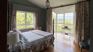 A bedroom with a large bed, two windows, a table with books, and a chair. - WATER FRONT SECRET GARDEN (ORTIGUEIRA)