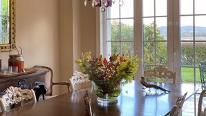 A dining area with a chandelier, a vase with flowers, and a view of greenery outside. - WATER FRONT SECRET GARDEN (ORTIGUEIRA)