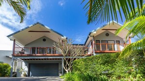Une maison à deux étages avec un garage, un balcon et une végétation luxuriante.