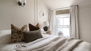 A neatly made bed with a patterned throw blanket, a bedside lamp, and a small table with a lamp and a vase. - Luxury Cottage with Parking, Minutes to Beach and Restaurants (Porthleven)