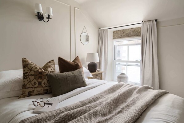 A neatly made bed with a patterned throw blanket, a bedside lamp, and a small table with a lamp and a vase. - Luxury Cottage with Parking, Minutes to Beach and Restaurants (Porthleven)
