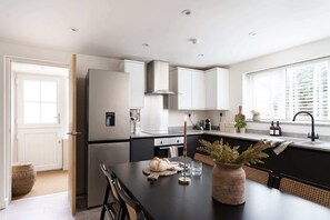 A modern kitchen with a central island, stainless steel appliances, and a window with blinds. - Luxury Cottage with Parking, Minutes to Beach and Restaurants (Porthleven)