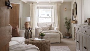 A cozy bedroom with a large window, a white sofa, a chair, a bedside table with a lamp, and a dresser. - Luxury Cottage with Parking, Minutes to Beach and Restaurants (Porthleven)