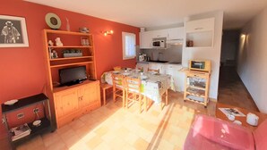 A compact living space with a dining area, kitchenette, and a television in the corner.