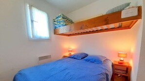 A bedroom with a bunk bed, a window with blinds, two bedside lamps, and a wooden headboard.