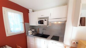 A compact kitchen with white cabinets, a microwave, a kettle, and a sink.