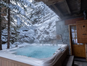 Relax in a hot tub surrounded by snow-covered trees and a rustic wooden structure.