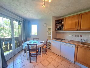 Een keuken met een eettafel, stoelen, een klok en uitzicht door de glazen deur.