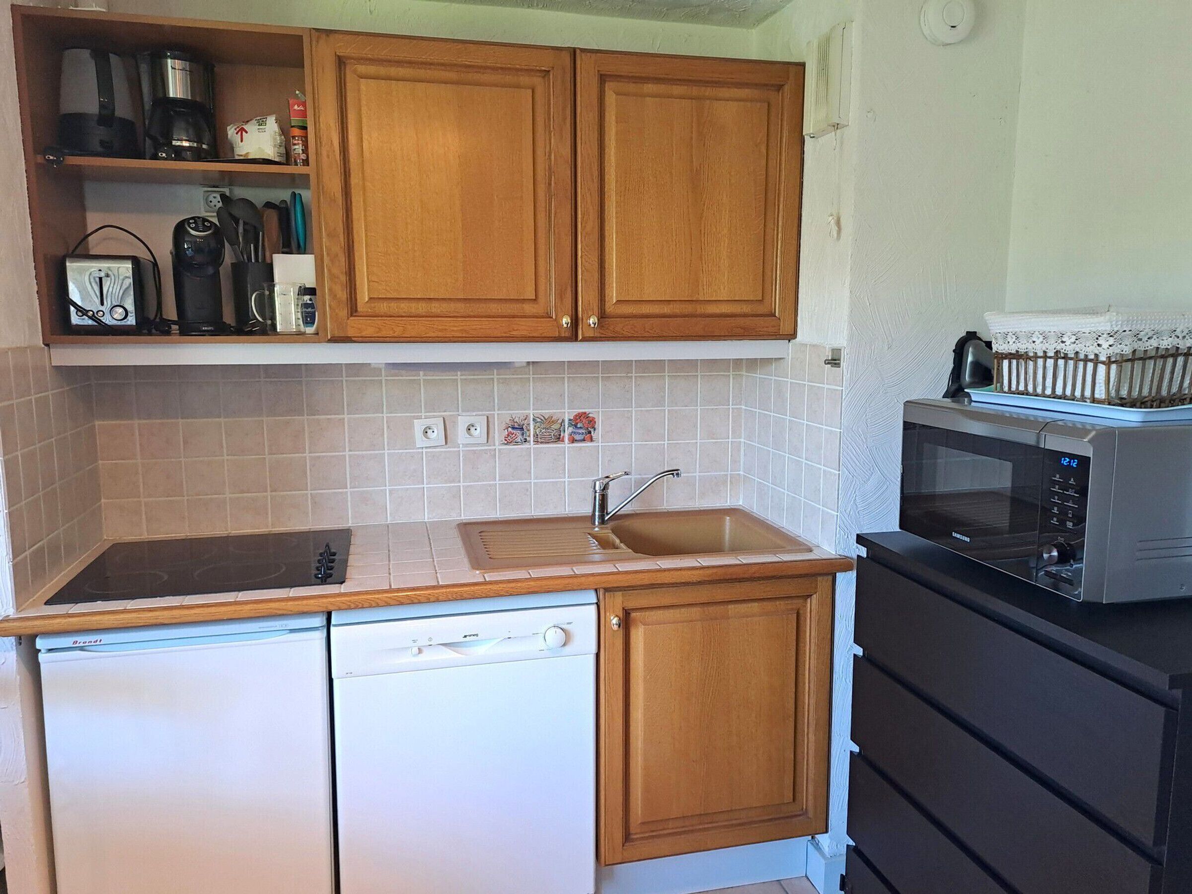 A compact kitchen with wooden cabinets, a built-in dishwasher, a microwave, and a sink.