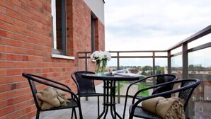 A balcony with a table and chairs, a white lantern, and a view of the city.