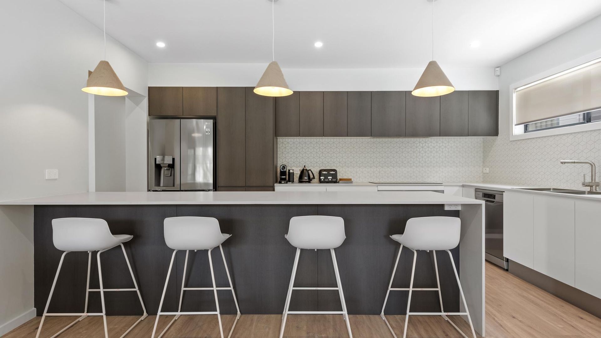 Een moderne keuken met een groot eiland, barstoelen en hanglampen.