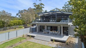 Een modern herenhuis met twee verdiepingen, een overdekt terras, een omheinde achtertuin en uitzicht op omliggende bomen.