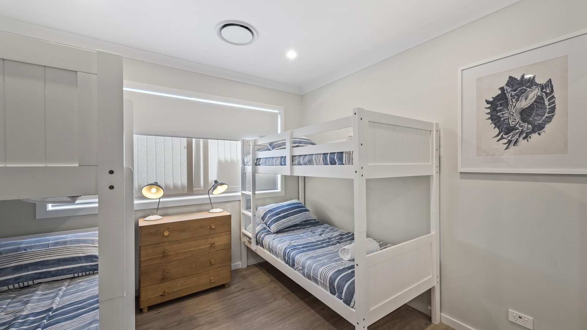 A child's bedroom with bunk beds, a wooden dresser, a desk with a lamp, and a framed artwork on the wall.