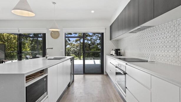 Una cocina moderna con una isla grande, horno empotrado y vistas al exterior a través de amplias puertas correderas.