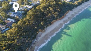 Vista aérea de una zona costera con un bosque denso, una playa de arena y un océano azul cristalino.
