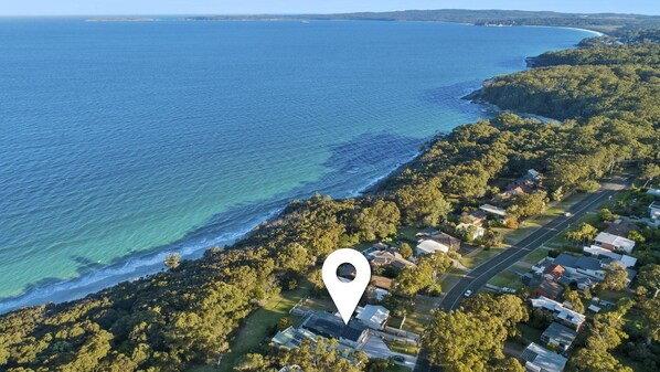 Vue aérienne d’une zone résidentielle côtière, avec des maisons, une route et une plage.