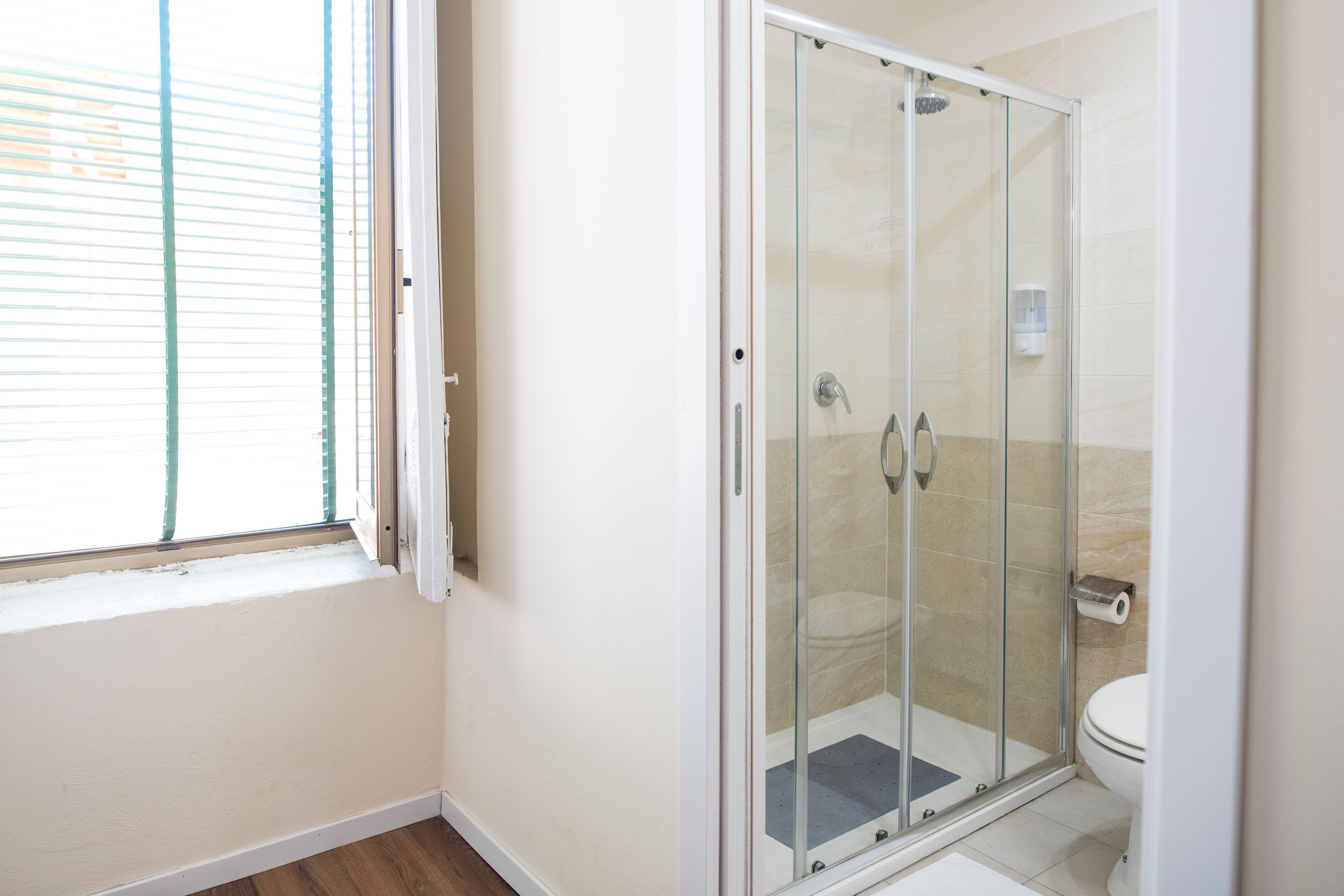 Un bagno con doccia vetro-muraria, un water e una finestra con persiane.