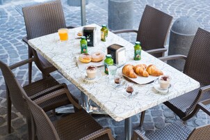 A breakfast table with croissants, pastries, and beverages, surrounded by wicker chairs.