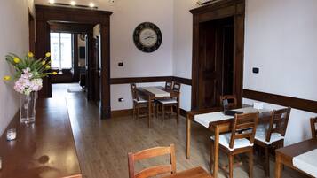Un'area pranzo con tavoli e sedie in legno, un orologio appeso al muro e un vaso con fiori su un tavolo.