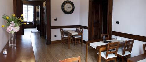A dining area with wooden tables and chairs, a clock on the wall, and a vase with flowers on a table.