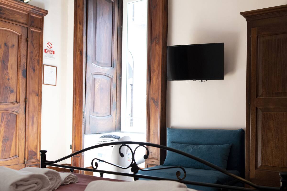 A bedroom with a bed, a TV mounted on the wall, wooden wardrobes, and a window.