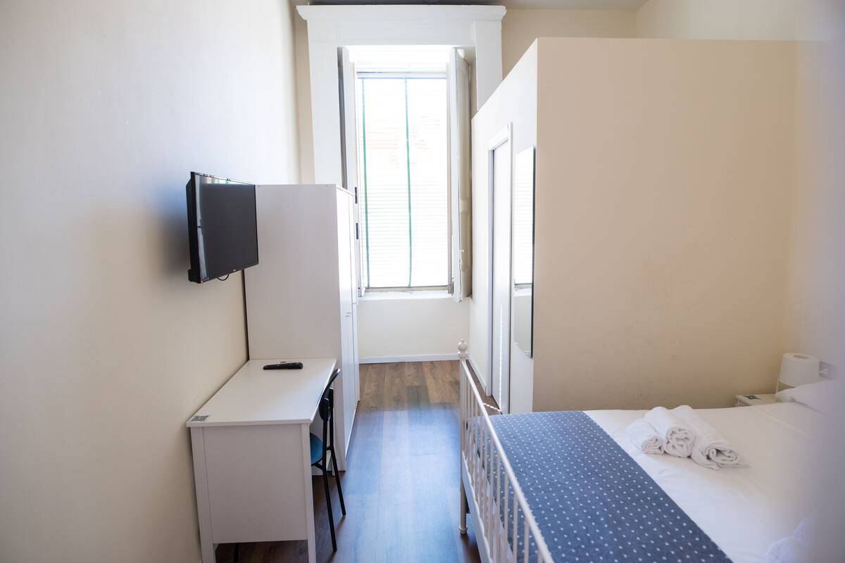 A hotel room with a bed, a desk, a TV, and a window.