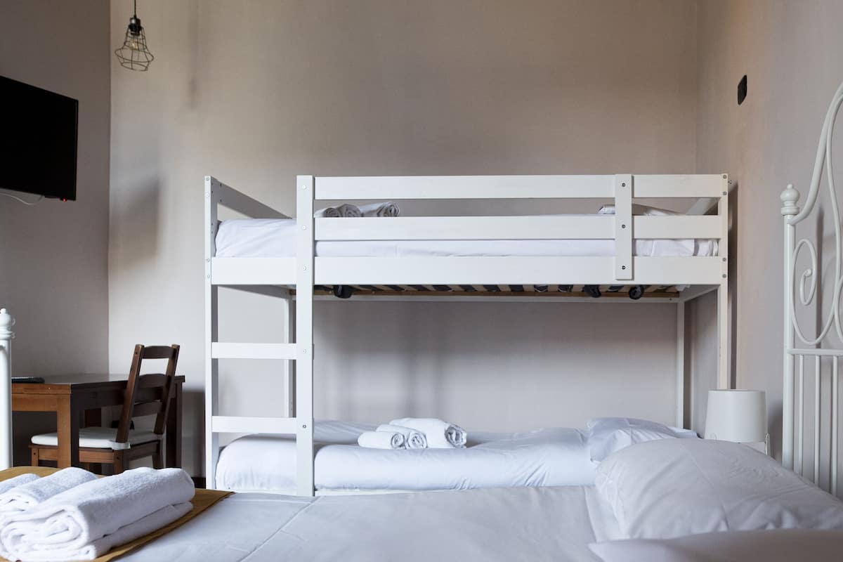 A bunk bed room with a desk and chair, a lamp, and a decorative metal headboard.