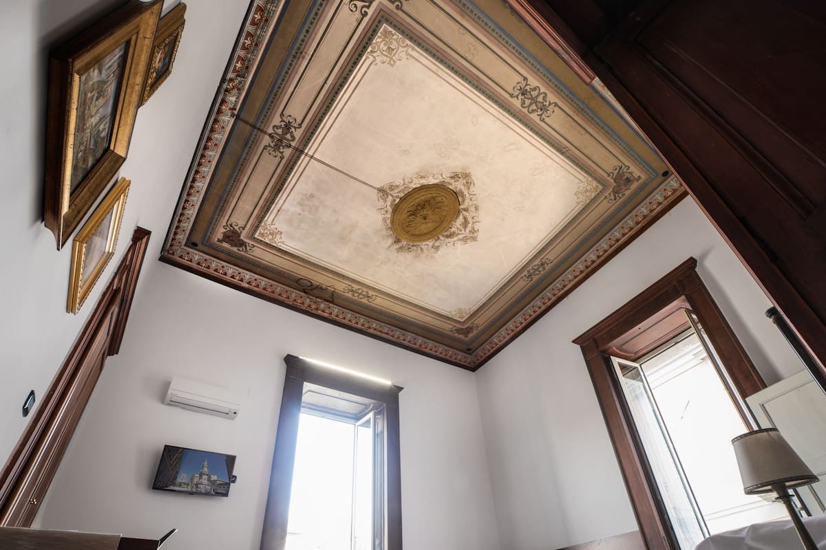A room with a high ceiling, ornate moldings, a framed picture, a door, and a window.