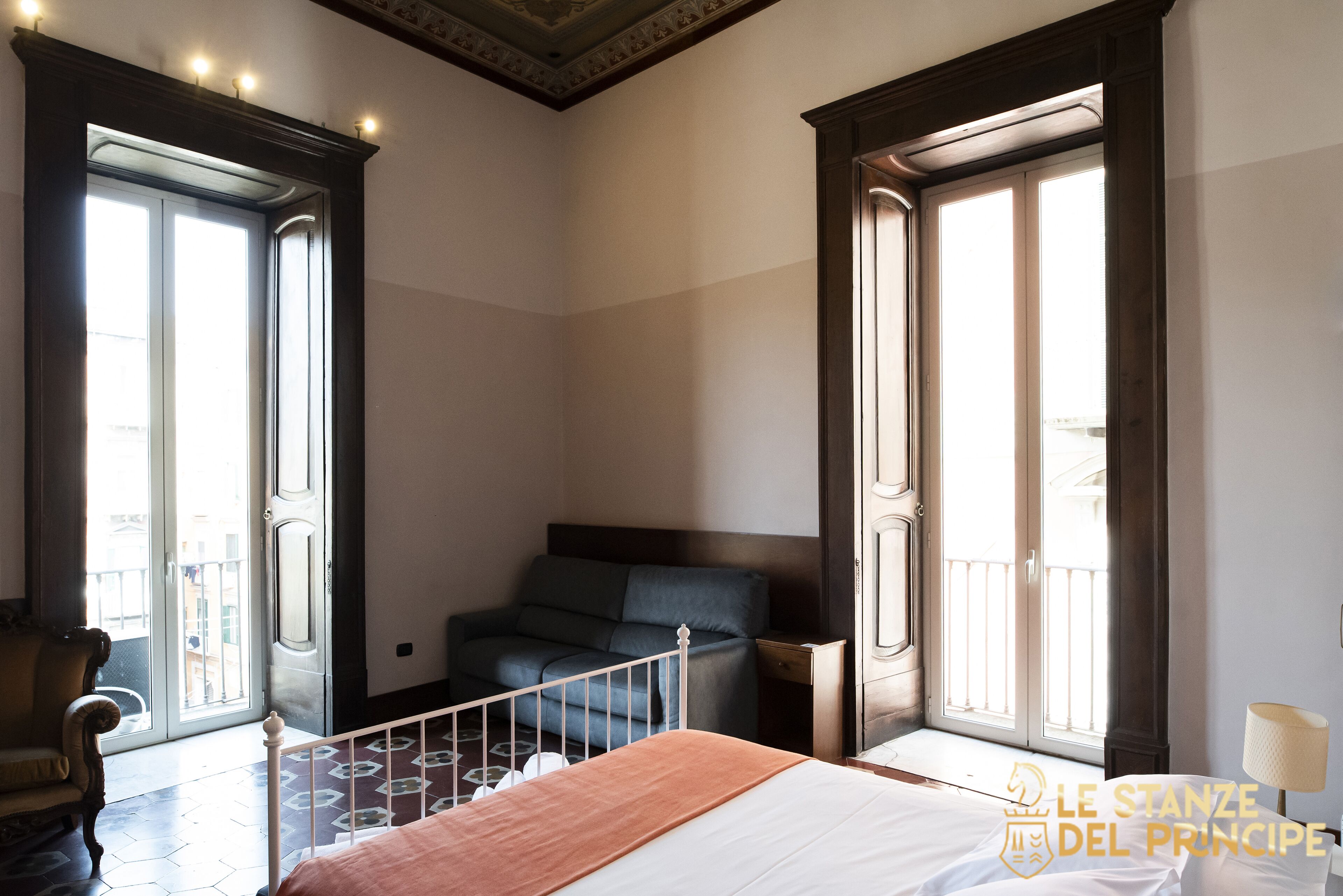 A hotel room with a bed, a sofa, a chair, and a balcony with a railing.