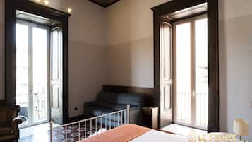 A hotel room with a bed, a sofa, a chair, and a balcony with a railing.