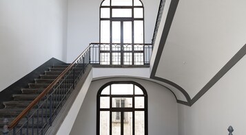A staircase with a wooden handrail and metal balusters, leading to a landing with a large arched window.