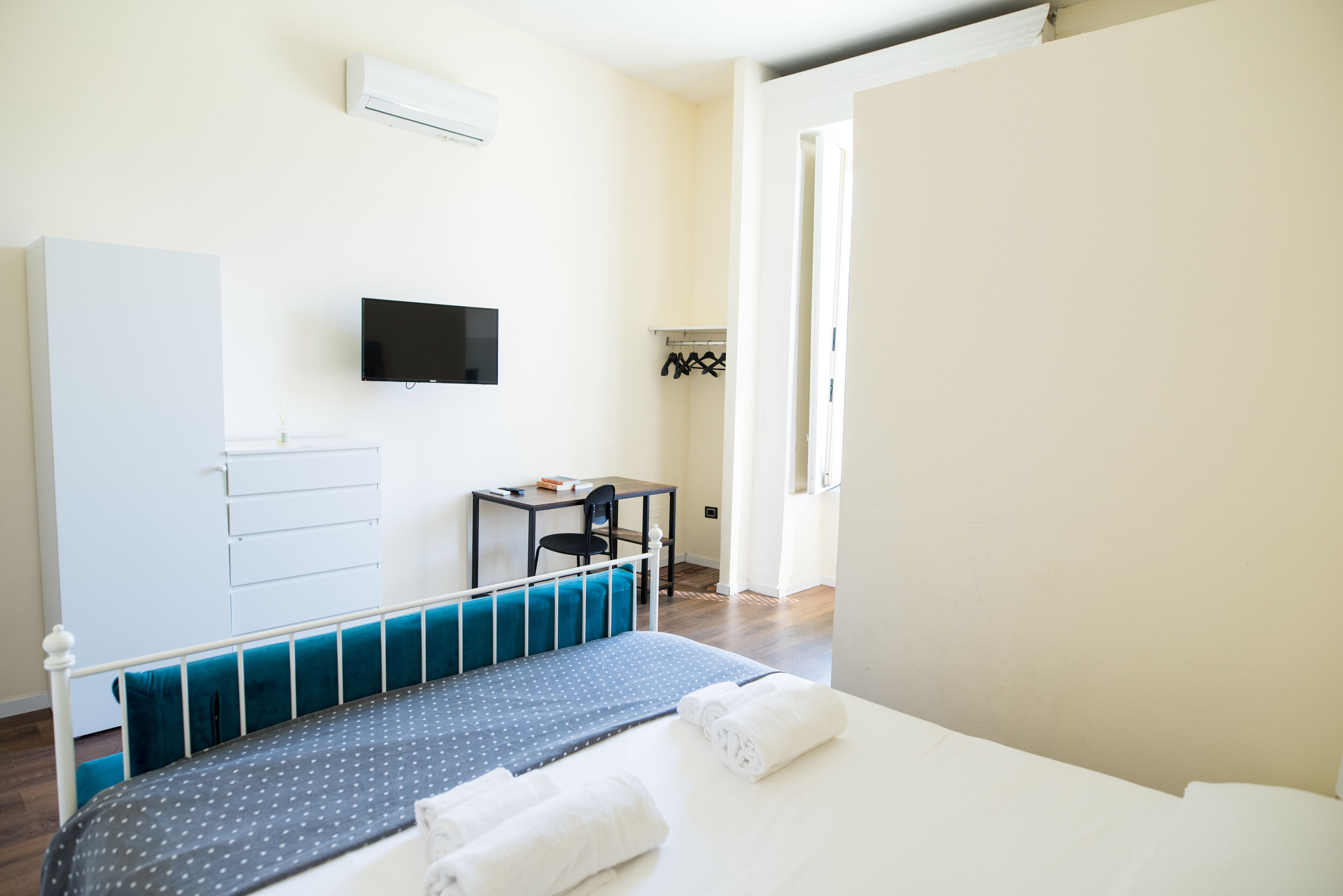 Una camera d'albergo con un letto, una scrivania, una sedia, una TV e un armadio.