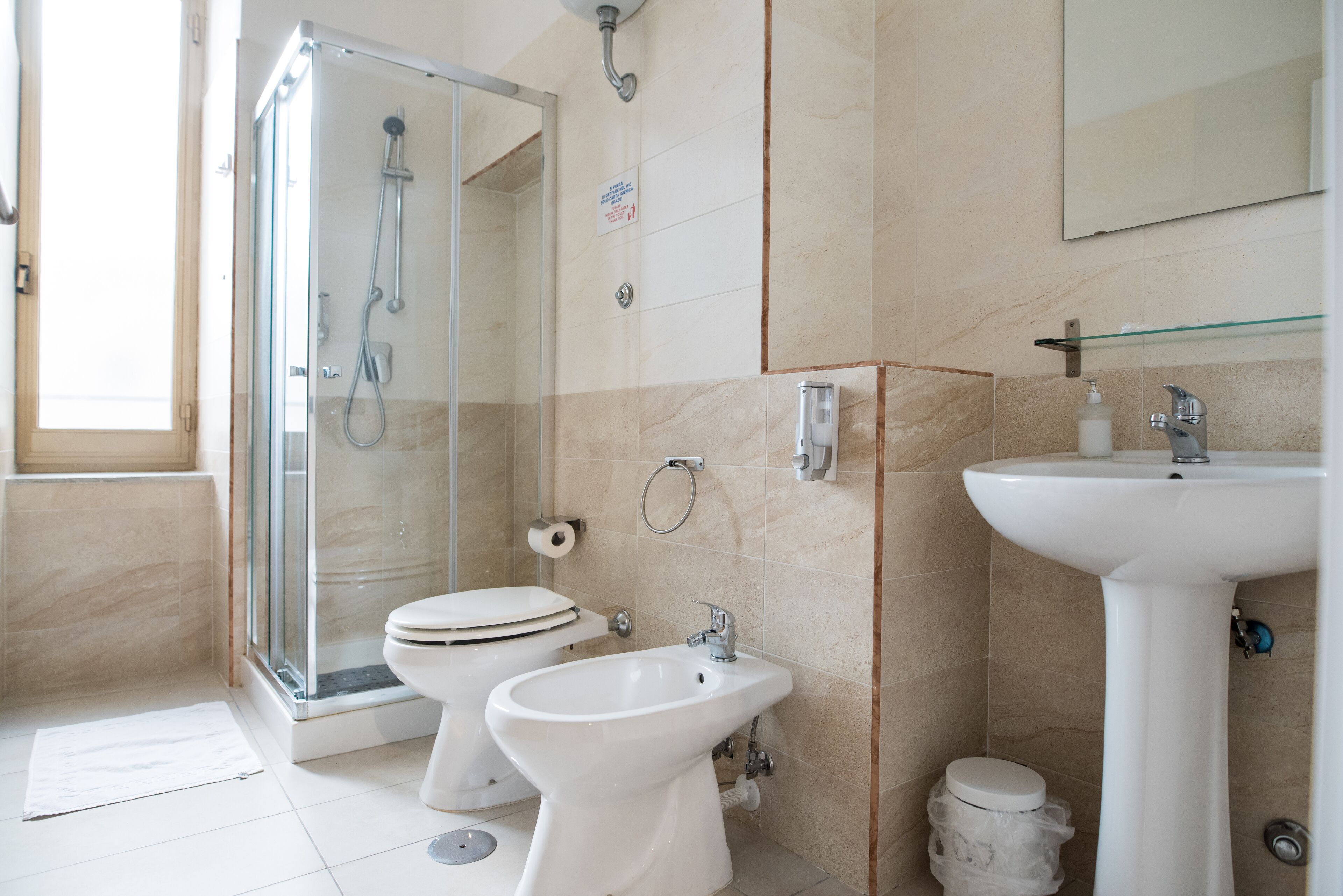 A bathroom with a glass-enclosed shower, a toilet, a bidet, and a sink.