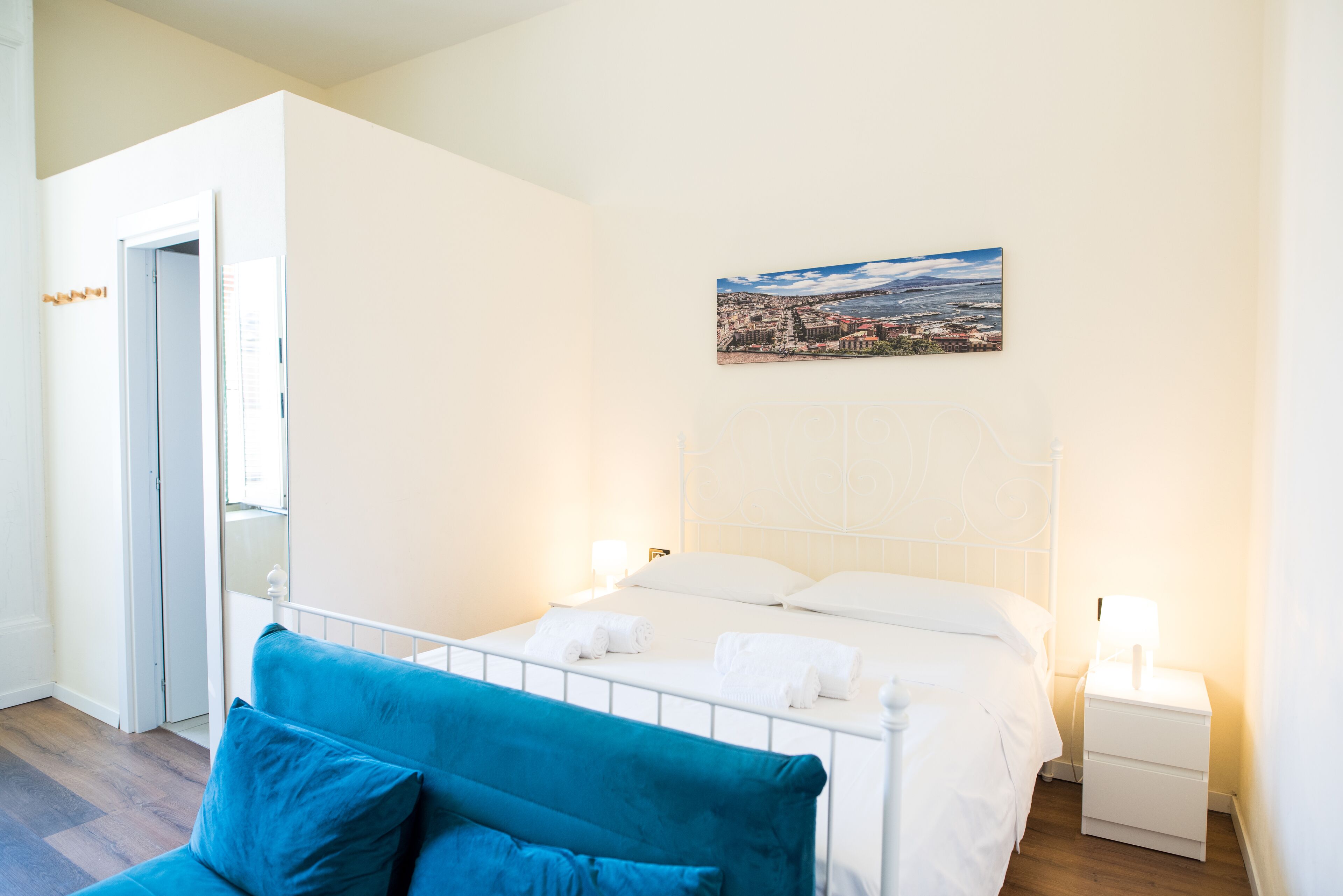 A hotel room with a bed, a blue sofa, a nightstand, and a painting on the wall.