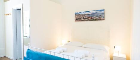 A hotel room with a bed, a blue sofa, a nightstand, and a painting on the wall.