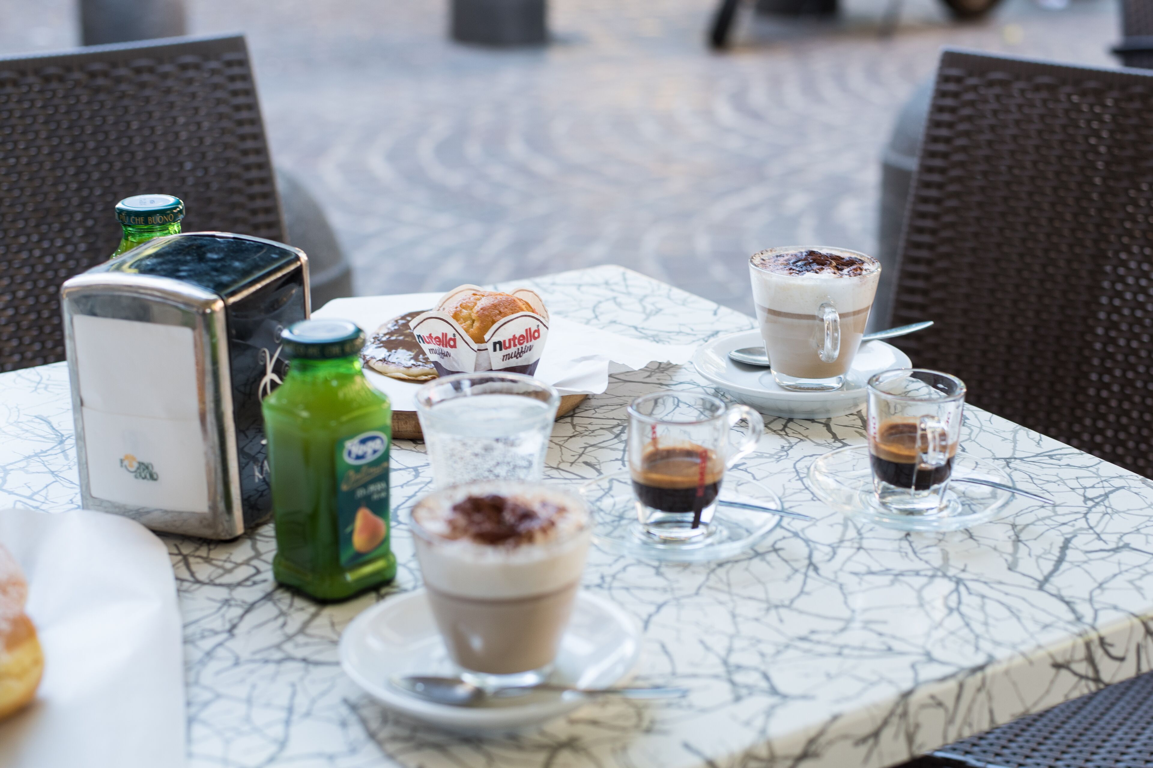 Una mesa con un croissant de Nutella, un frasco de Nutella, una botella verde y dos tazas de café con crema batida.