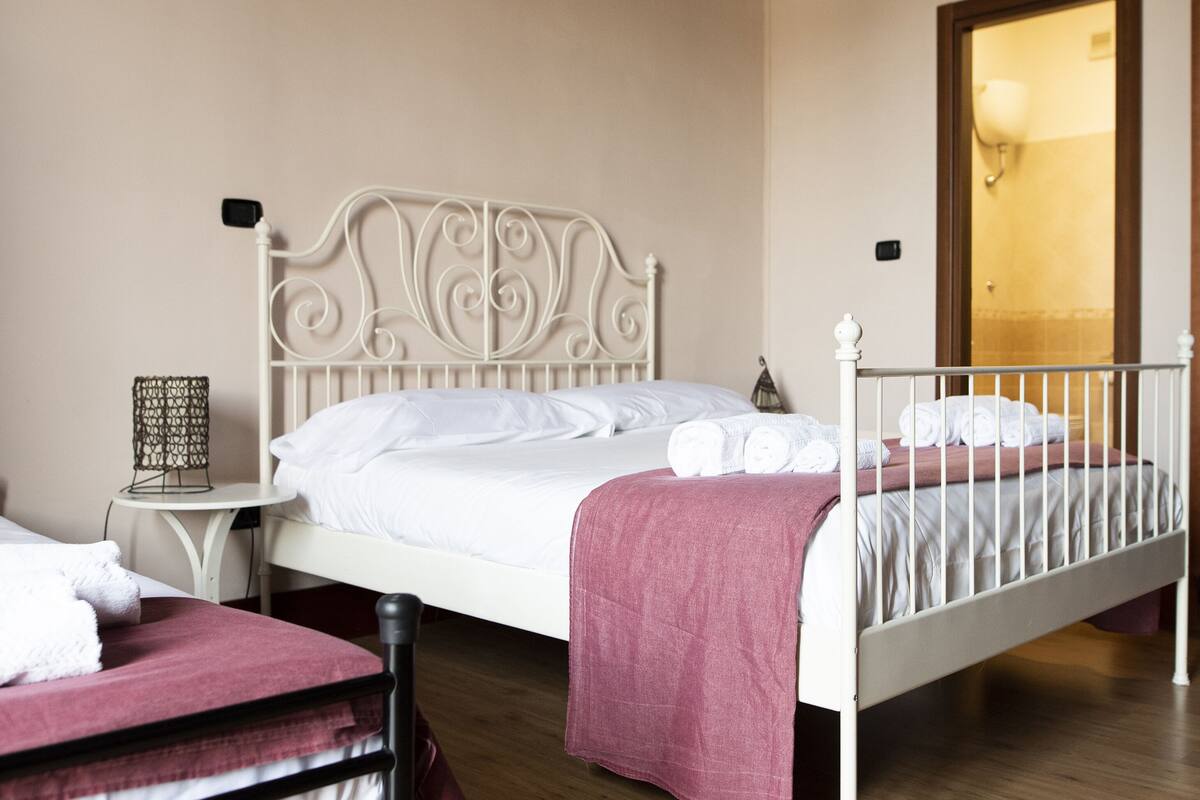 A hotel room with a single bed, a bedside table with a lamp, and a bunk bed in the corner.