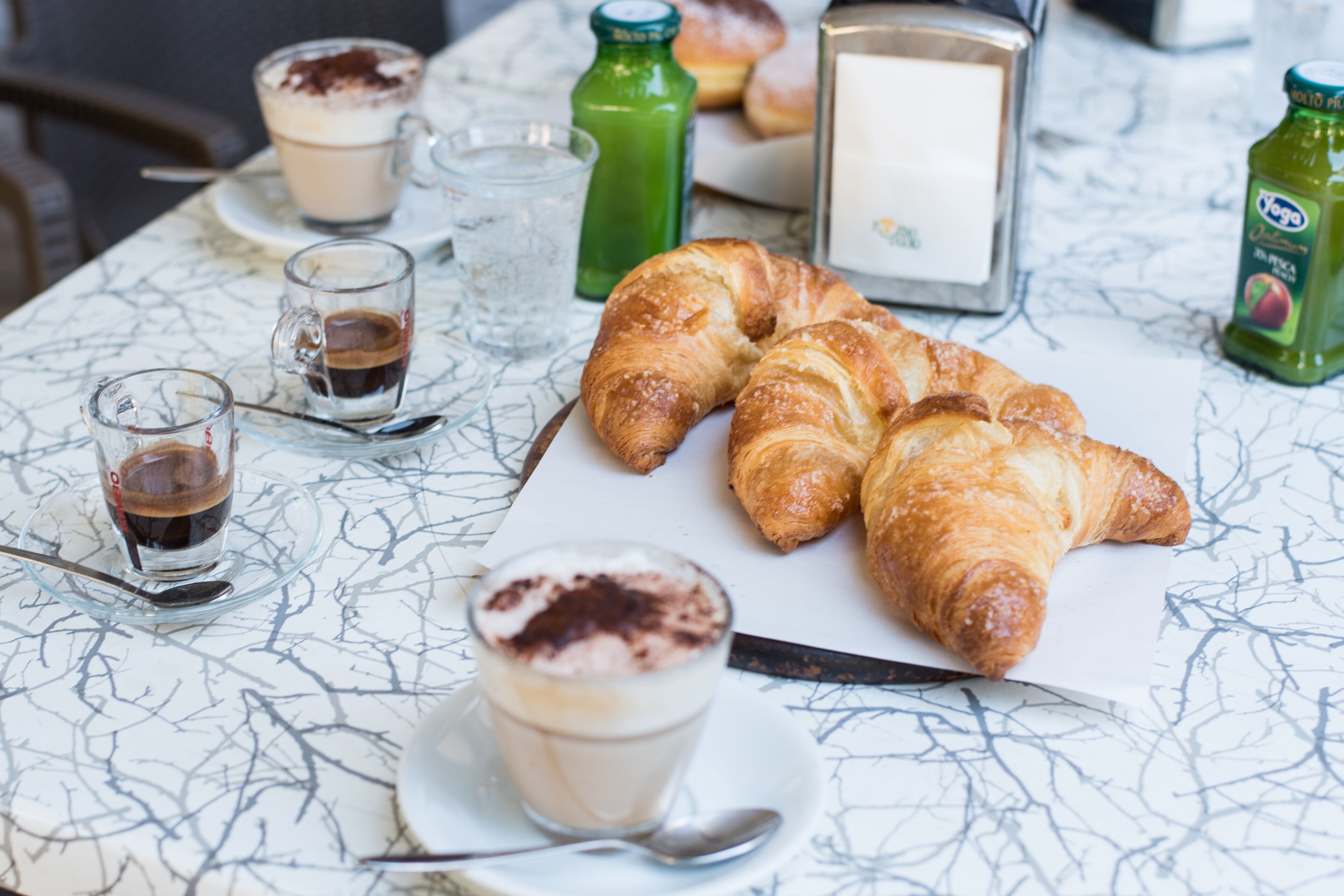 Una mesa con cruasanes, café y un vaso de leche.