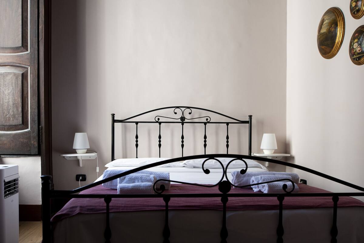 A neatly made bed with a metal headboard, two bedside lamps, and a wall-mounted picture frame.