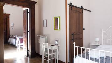 Een slaapkamer met een houten deur, een wit bed, een wit bureau met stoel en een radiator.